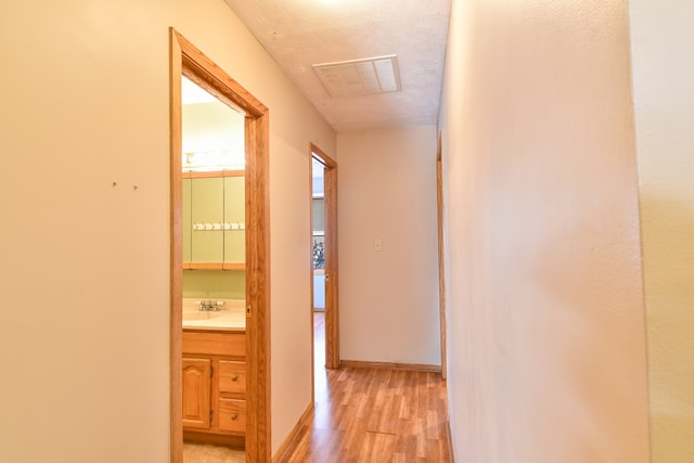 corridor with sink, a textured ceiling, and light wood-type flooring