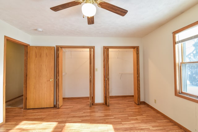 unfurnished bedroom featuring ceiling fan, two closets, a textured ceiling, and light wood-type flooring