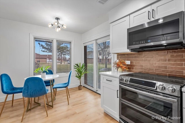 kitchen with backsplash, stainless steel appliances, an inviting chandelier, white cabinets, and light hardwood / wood-style floors