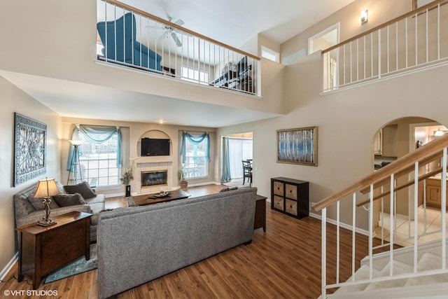 living room with hardwood / wood-style flooring, ceiling fan, a towering ceiling, and a tiled fireplace