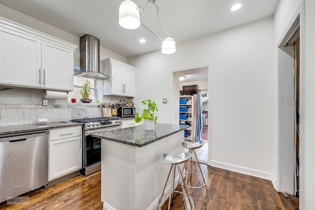 kitchen with wall chimney exhaust hood, dark stone countertops, white cabinetry, and stainless steel appliances