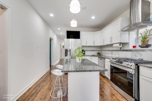 kitchen featuring a center island, white cabinets, wall chimney range hood, decorative backsplash, and appliances with stainless steel finishes