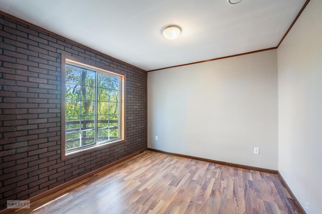 empty room with ornamental molding, brick wall, and wood-type flooring