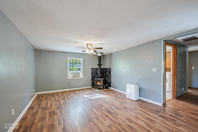 unfurnished living room featuring hardwood / wood-style floors, a textured ceiling, a wood stove, and ceiling fan