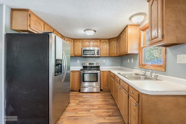 kitchen with a textured ceiling, light wood-type flooring, sink, and appliances with stainless steel finishes