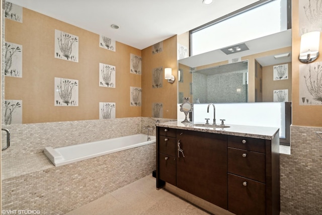 bathroom with tile walls, tiled bath, tile patterned floors, and vanity