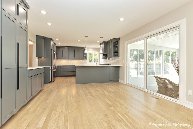 kitchen featuring light hardwood / wood-style flooring, gray cabinets, stainless steel fridge, tasteful backsplash, and decorative light fixtures