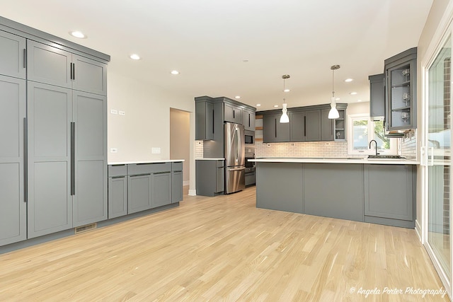 kitchen with decorative backsplash, stainless steel fridge, light hardwood / wood-style floors, decorative light fixtures, and gray cabinets