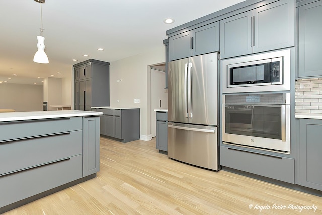 kitchen featuring hanging light fixtures, gray cabinets, tasteful backsplash, light hardwood / wood-style floors, and stainless steel appliances