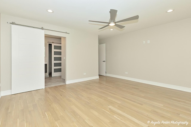 unfurnished room featuring a barn door, light hardwood / wood-style floors, and ceiling fan