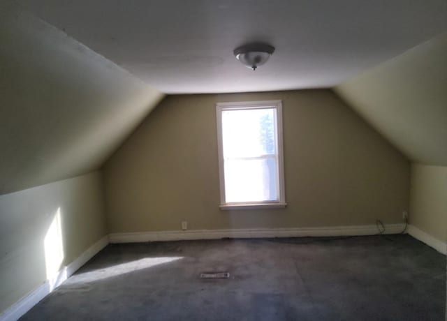 additional living space with dark carpet and vaulted ceiling