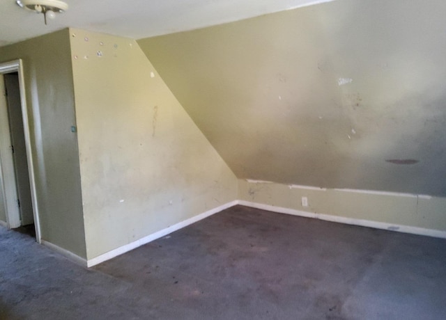 additional living space with dark colored carpet and lofted ceiling