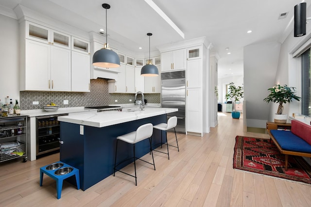 kitchen with stainless steel built in refrigerator, beverage cooler, sink, white cabinetry, and an island with sink