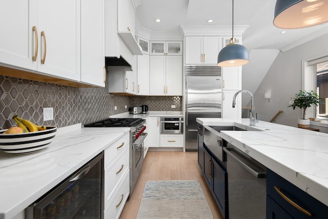 kitchen featuring high end appliances, beverage cooler, sink, decorative light fixtures, and white cabinetry