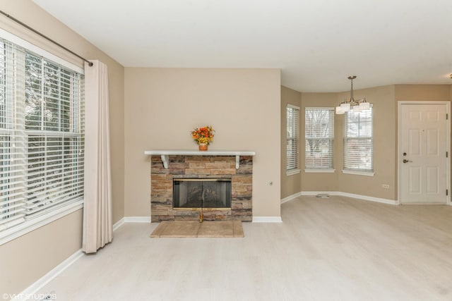 unfurnished living room featuring light wood-type flooring, a stone fireplace, an inviting chandelier, and plenty of natural light