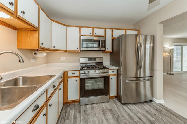 kitchen with white cabinets, light wood-type flooring, appliances with stainless steel finishes, and sink