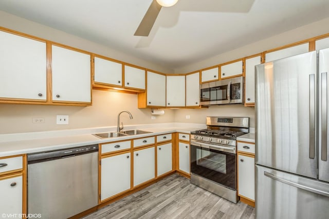 kitchen featuring appliances with stainless steel finishes, white cabinetry, sink, light wood-type flooring, and ceiling fan