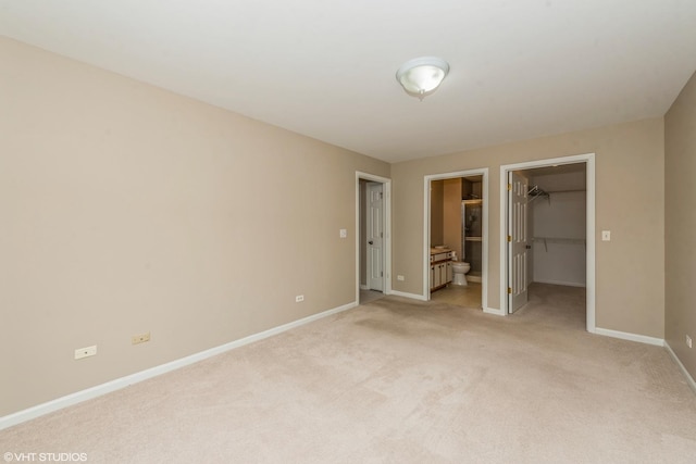 unfurnished bedroom featuring light carpet, a closet, connected bathroom, and a spacious closet