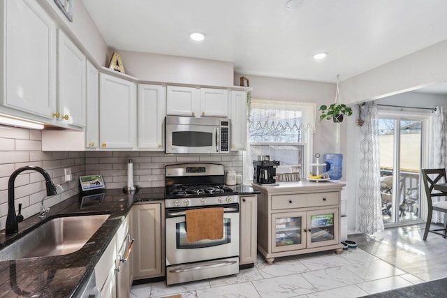 kitchen featuring sink, tasteful backsplash, white cabinetry, dark stone counters, and stainless steel appliances