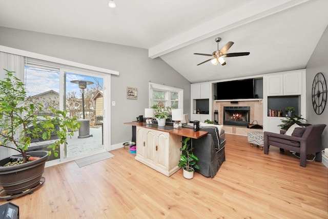 living room featuring a tiled fireplace, ceiling fan, vaulted ceiling with beams, and light wood-type flooring