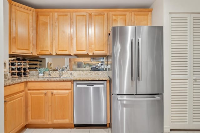 kitchen with light stone countertops, stainless steel appliances, light brown cabinetry, sink, and light tile patterned floors