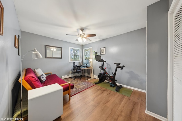 workout area featuring ceiling fan, a baseboard heating unit, and hardwood / wood-style flooring