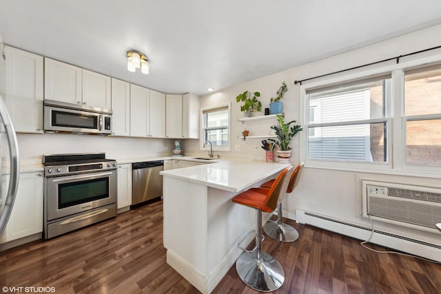 kitchen with kitchen peninsula, sink, baseboard heating, appliances with stainless steel finishes, and white cabinetry