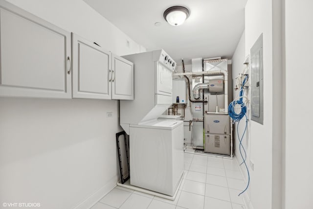 laundry room featuring cabinets, light tile patterned floors, tankless water heater, and stacked washer and clothes dryer