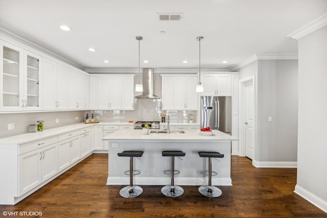 kitchen featuring appliances with stainless steel finishes, wall chimney exhaust hood, sink, white cabinetry, and hanging light fixtures