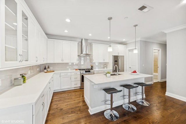 kitchen with dark wood-type flooring, a center island with sink, wall chimney exhaust hood, appliances with stainless steel finishes, and white cabinetry