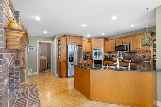 kitchen featuring appliances with stainless steel finishes, dark stone counters, decorative backsplash, sink, and light hardwood / wood-style flooring