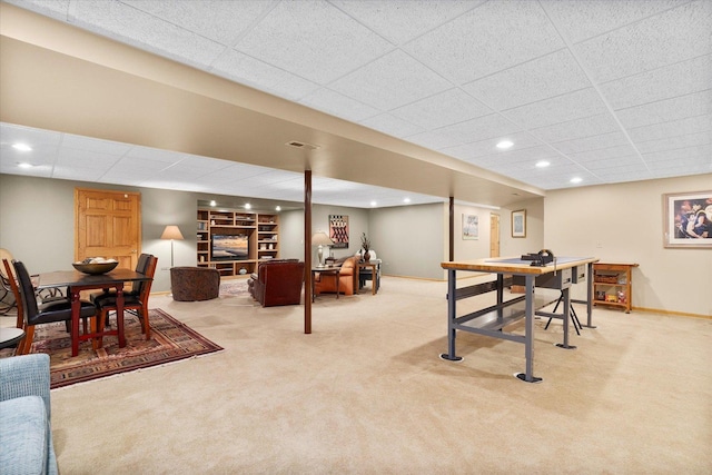 recreation room featuring built in features, light carpet, and a drop ceiling