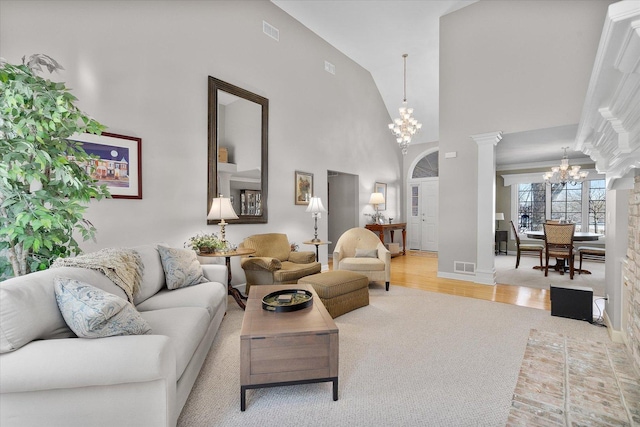 living room featuring a towering ceiling, decorative columns, an inviting chandelier, and hardwood / wood-style floors