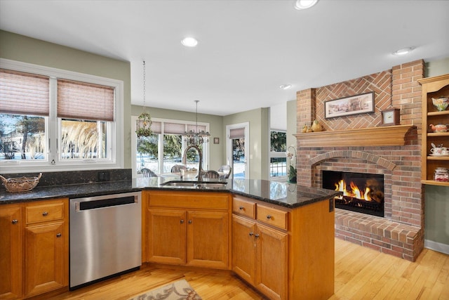 kitchen with sink, dark stone countertops, stainless steel dishwasher, a brick fireplace, and pendant lighting