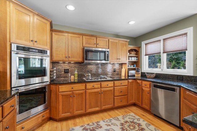 kitchen featuring stainless steel appliances, dark stone countertops, light hardwood / wood-style flooring, and decorative backsplash