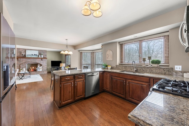 kitchen with sink, a fireplace, dark hardwood / wood-style flooring, kitchen peninsula, and stainless steel appliances