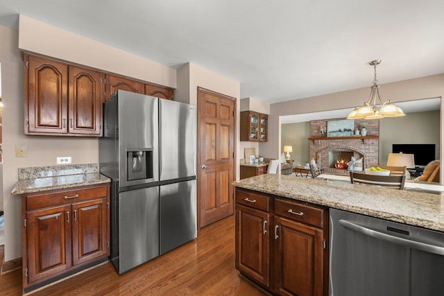 kitchen featuring light stone countertops, hanging light fixtures, stainless steel appliances, dark hardwood / wood-style floors, and a fireplace