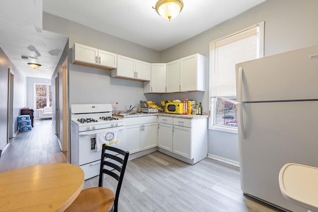 kitchen with white appliances, white cabinets, sink, light hardwood / wood-style flooring, and light stone counters