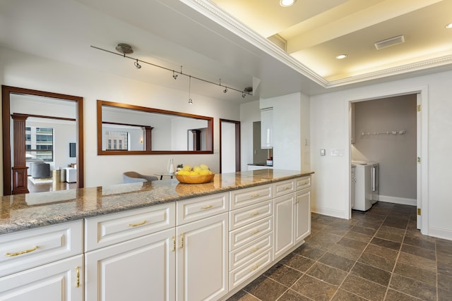 kitchen with light stone counters, a raised ceiling, crown molding, independent washer and dryer, and white cabinetry