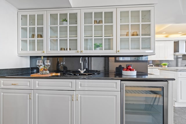 bar with white cabinetry, wall chimney exhaust hood, beverage cooler, dark stone counters, and decorative backsplash