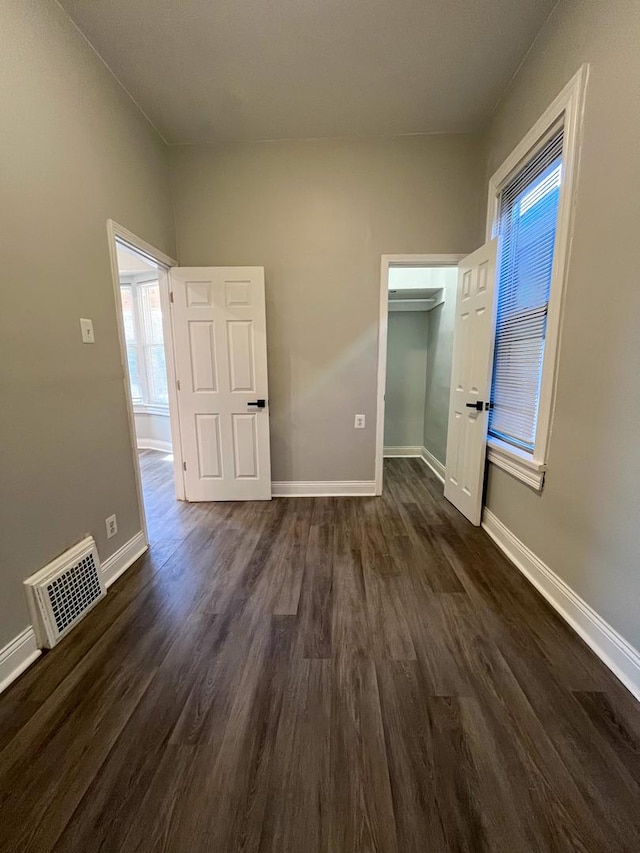 unfurnished bedroom with a walk in closet, a closet, and dark wood-type flooring