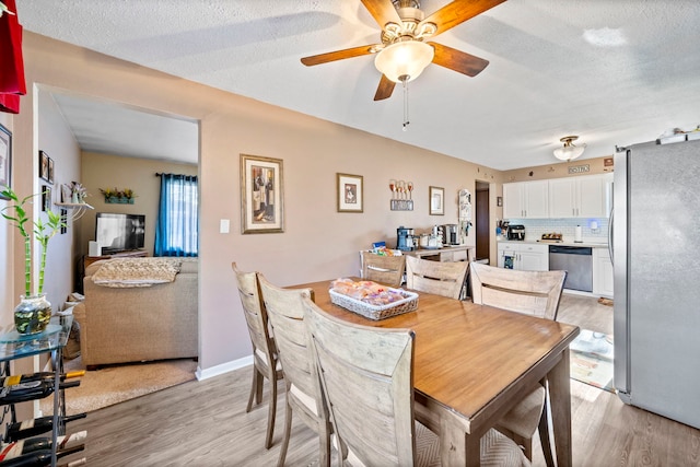 dining area with a textured ceiling, ceiling fan, and light hardwood / wood-style flooring