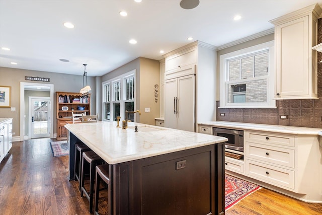 kitchen with pendant lighting, sink, backsplash, a center island with sink, and built in appliances