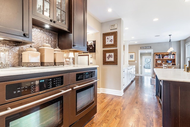 kitchen with ornate columns, decorative backsplash, dark brown cabinets, decorative light fixtures, and light wood-type flooring