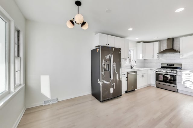 kitchen featuring pendant lighting, appliances with stainless steel finishes, wall chimney exhaust hood, and white cabinetry