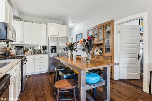 kitchen featuring dark hardwood / wood-style floors, light stone countertops, white cabinetry, and stainless steel appliances