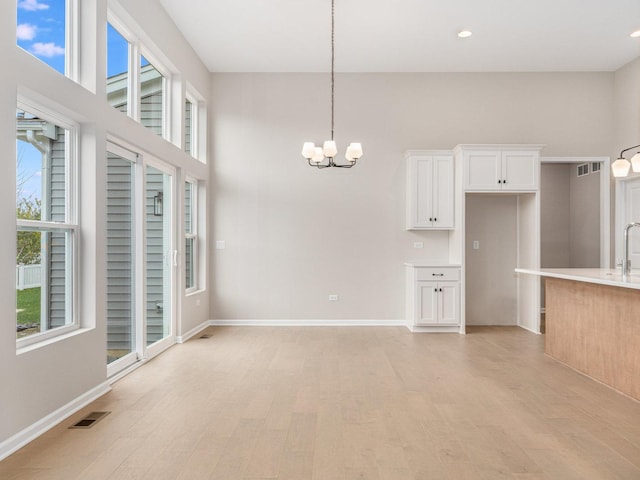 kitchen featuring a high ceiling, white cabinets, an inviting chandelier, hanging light fixtures, and light wood-type flooring