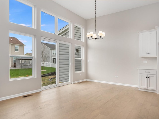 unfurnished dining area with light hardwood / wood-style floors, plenty of natural light, and a notable chandelier