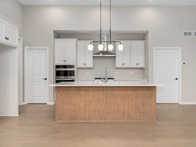 kitchen with white cabinets, light hardwood / wood-style floors, hanging light fixtures, and an island with sink