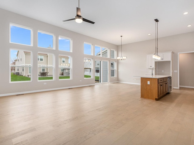 unfurnished living room with a healthy amount of sunlight, ceiling fan with notable chandelier, and light hardwood / wood-style flooring